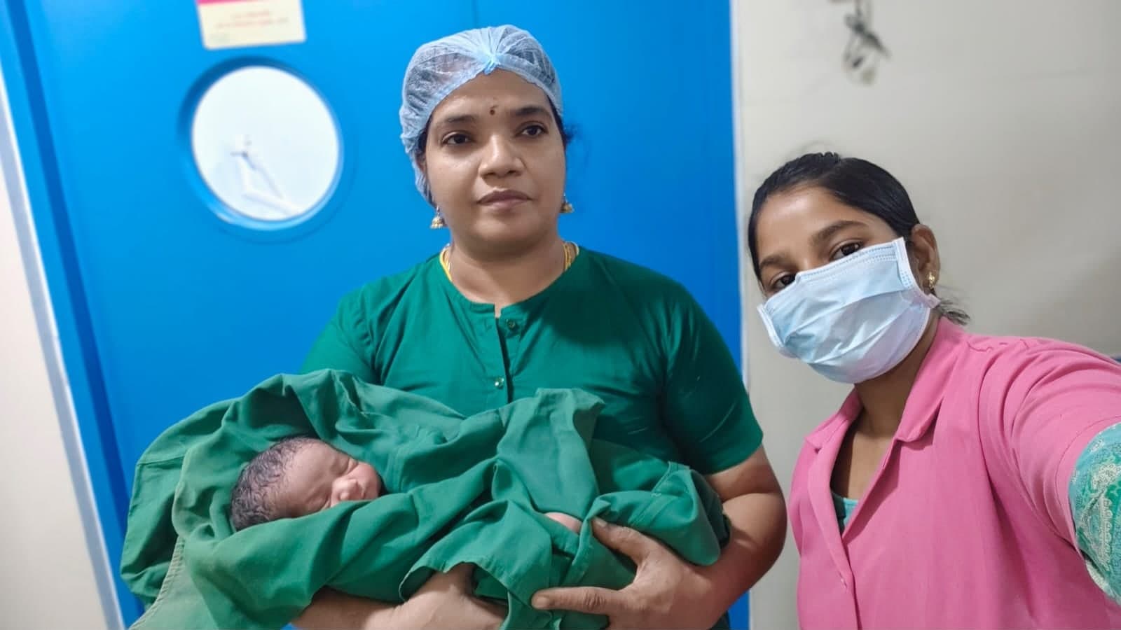 Dr. Sangeetha Balamurugan in theatre scrubs holding a newborn, beside a member of the care team