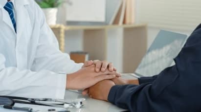 A doctor holding a patient's hands during a consultation