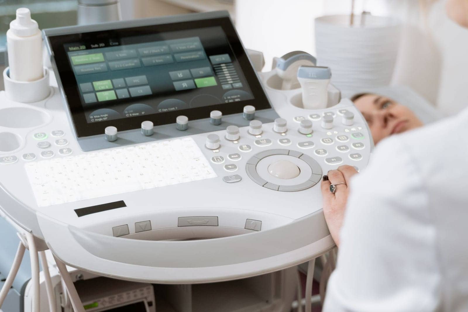 An ultrasound machine in a consultation room, with a patient on the examination couch
